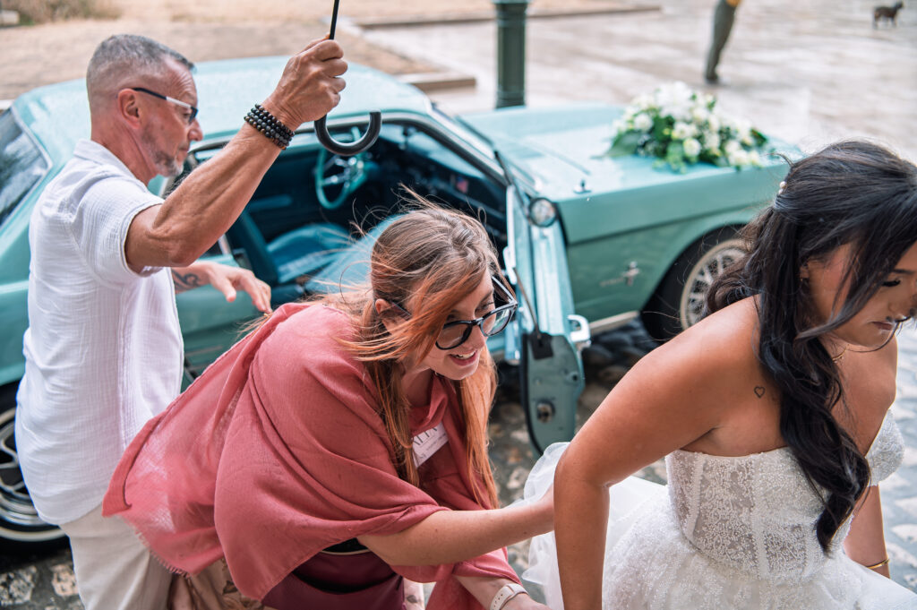 Alia Wedding planner qui aide la mariée avec sa robe de mariée devant une mustang verte